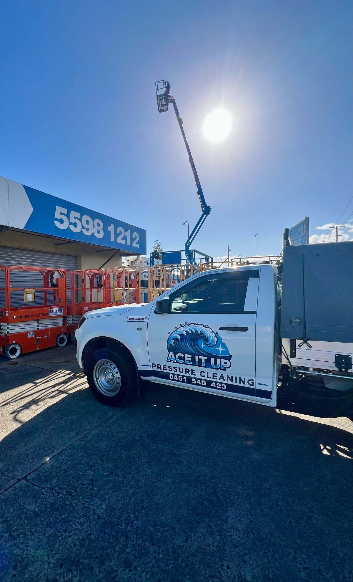White pressure cleaning truck with cherry picker arm parked at construction site under bright sun