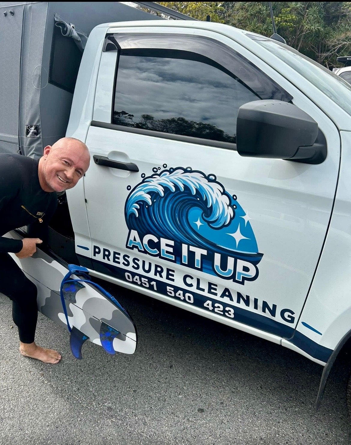 Man in black shirt posing next to white service truck with Ace It Up Pressure Cleaning logo and blue wave design